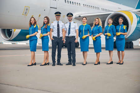 Handsome pilots and beautiful stewardesses standing outdoors in airfieldの写真素材