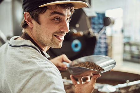 Handsome young man holding scoop with coffee beans