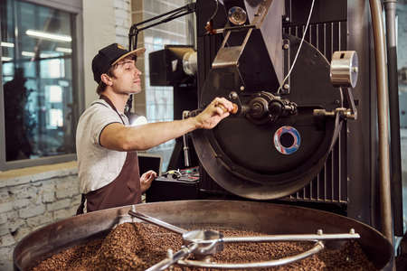 Handsome young man using industrial coffee roasting machineの写真素材