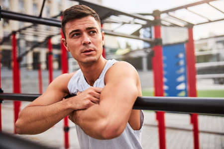 Strong handsome guy training alone on sports ground