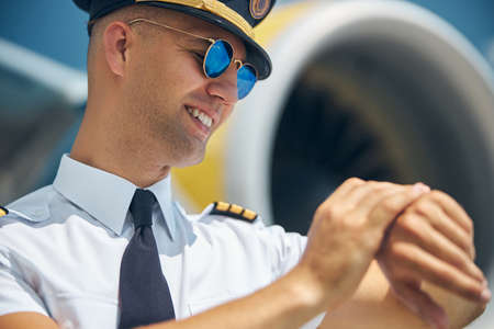 Cheerful male pilot looking at wristwatch at airfieldの写真素材