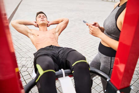 Muscular man training abdominal with girlfriend support outdoorsの写真素材