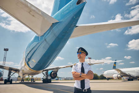 Cheerful male pilot in sunglasses standing outdoors in airfield