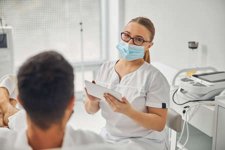 Female esthetician with tablet computer talking with male patientの写真素材