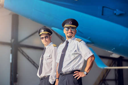 Happy smiling men in sunglasses standing in the hangar at the airportの写真素材