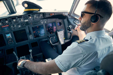 Beaming man in uniform sitting on the chair in cockpit of passenger airplaneの写真素材