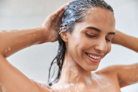 Joyful young woman washing her hair in showerの写真素材
