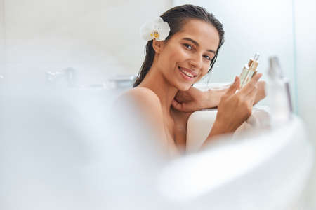 Attractive young woman holding vitamin serum while taking bathの写真素材
