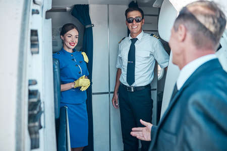 Smiling crew meeting businessman on passenger planeの写真素材