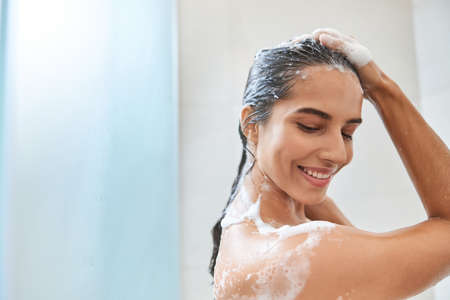 Charming young woman washing her hair in showerの写真素材