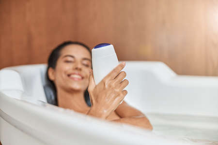 Charming young woman holding shower gel while taking bath