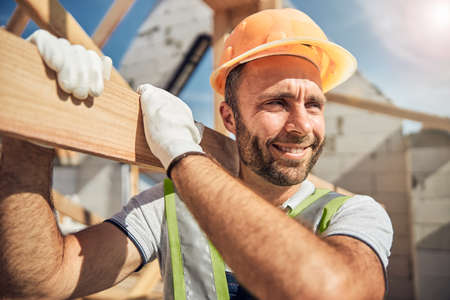Positive delighted young constructor carrying wooden beamの写真素材