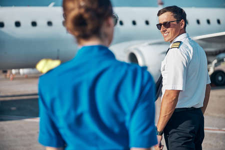 Cheerful handsome pilot with stewardess walking to jetの写真素材