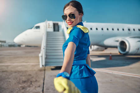Smiling pretty stewardess on runway near planeの写真素材