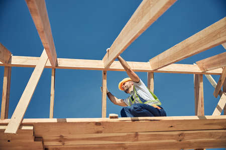 Attentive bearded constructor fixing two beams on the roofの写真素材