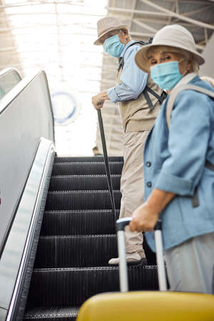 Two senior people in face masks on the moving staircase