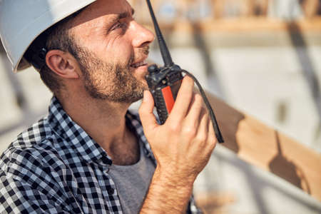 Gladsome builder holding a walkie-talkie close to his mouthの写真素材
