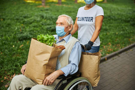Older male in medicine mask holding paper shopping bag on the legsの写真素材