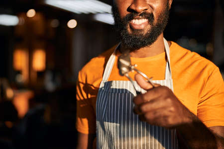 Close up of cheerful Afro American man with hair clipper in his hand standing in barbershopの写真素材