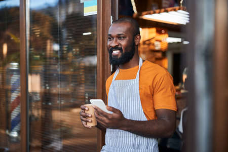 Cheerful male worker using smartphone and drinking coffee outdoorsの写真素材