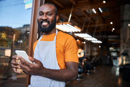 Cheerful Afro American man using smartphone outside barbershop