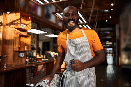 Cheerful Afro American man with hair trimmer standing in barbershopの写真素材