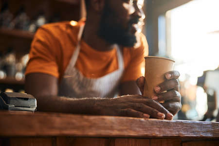 Male bartender with cup of coffee standing at the bar counterの写真素材