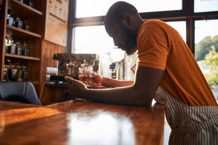 Handsome male bartender holding glass of whiskyの写真素材