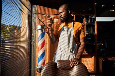 Handsome male barber in apron holding portable hair trimmerの写真素材