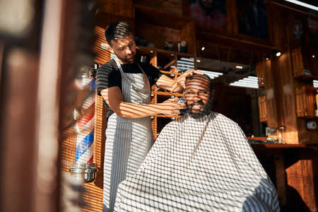 Male barber shaving client beard with electric razorの写真素材
