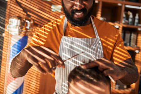 Smiling barber cutting man hair with professional scissorsの写真素材