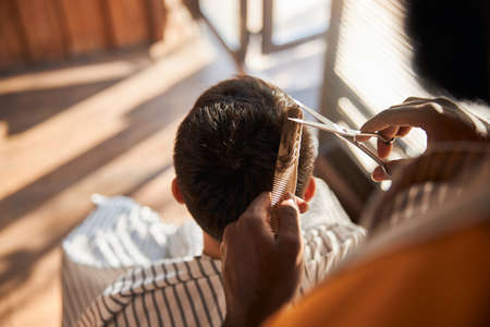 Barber cutting client hair with scissors in barbershop