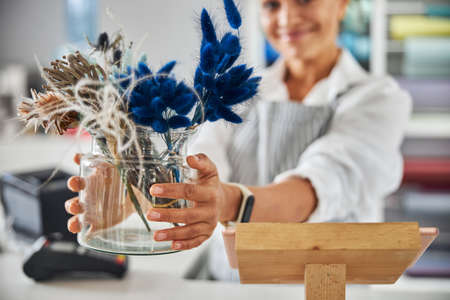 Pretty brunette woman showing a vase with flowers