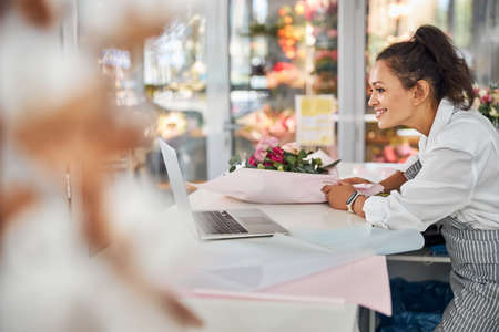 Professional flower shop worker with a bouquet looking at laptopの写真素材
