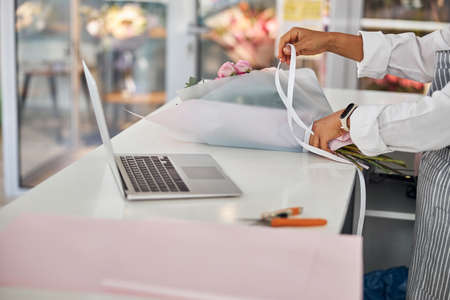 Experienced flower shop worker decorating a bouquet with a ribbonの写真素材