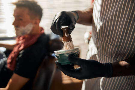 Male barber lathering shaving cream with brush