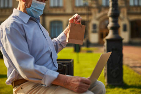 Old person holding laptop while sitting in the yardの写真素材