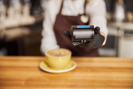 Barista standing near bar counter pay bill using cell application and pos machine