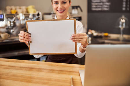Young female showing white paper at the photo camera in the indoorsの写真素材