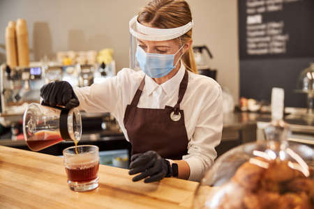 Blonde charming female in protective medicine mask working at the coffee barの写真素材