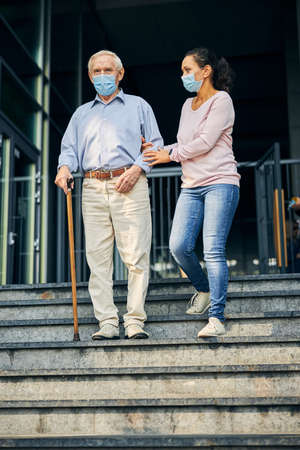 Young woman helping senior man coming down stairsの写真素材