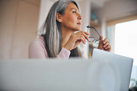 Beautiful woman holding glasses and using laptop at homeの写真素材