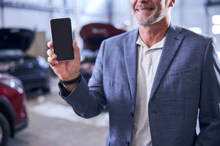 Bearded man holding modern smartphone and smiling