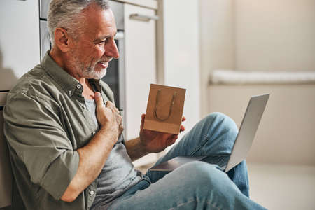 Thankful aged man holding a gift and a laptop