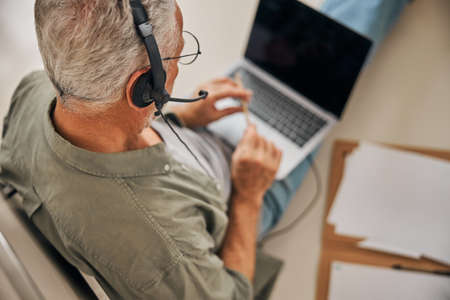 Busy aged gentleman in a headset holding a laptop