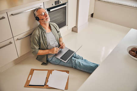 Busy elderly gentleman working remotely from his kitchenの写真素材