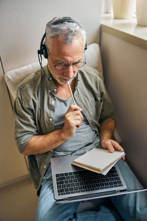 Focused aged man in glasses and headphones working from homeの写真素材