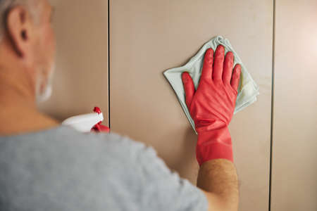 Neat aged gentleman wiping walls of his house clean