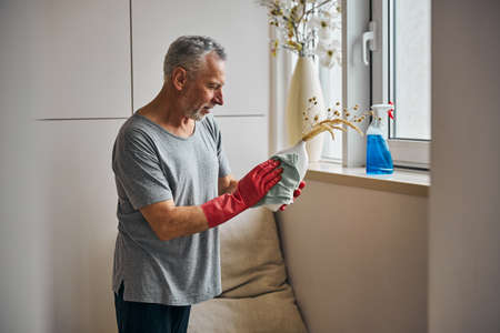 Focused senior citizen cleaning a vase with a wet wipeの写真素材