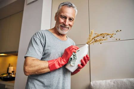 Cheerful aging man using wet cloth to clean his vaseの写真素材